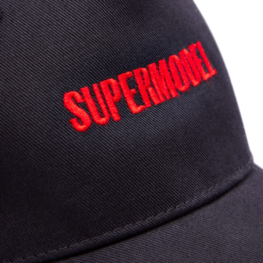 A detail of a baseball cap with the text 'supermodel' embroidered in bright red capital letters.